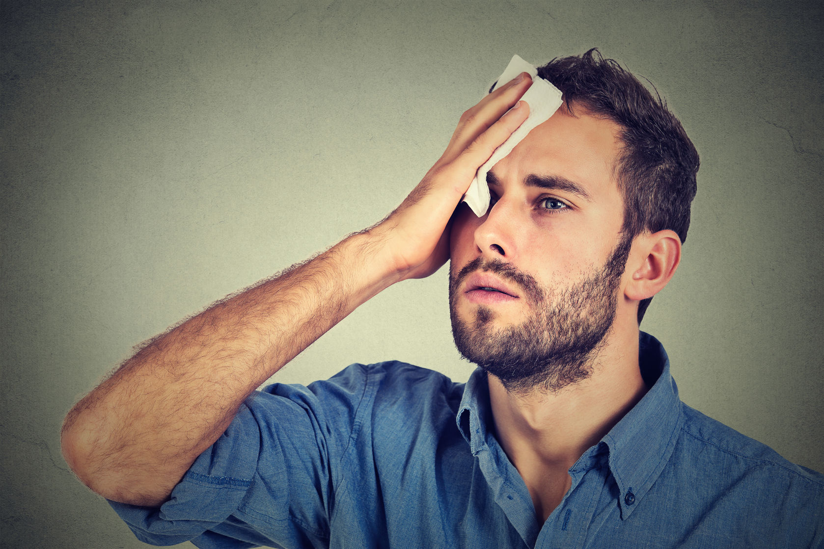 46737381 - tired man stressed sweating having fever headache isolated on gray wall background. worried guy wipes sweat on his face