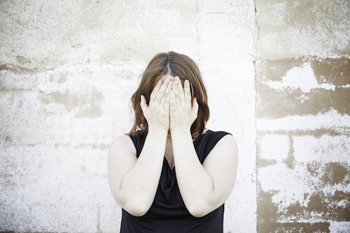 Girl covering face on urban street, people