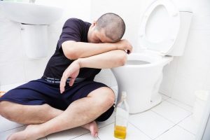Drunk fat man with wine bottle in toilet