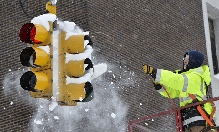 Cidade de Erie de Engenharia de Tráfego funcionário usa ar comprimido para limpar a neve de um sinal de trânsito City Of Erie Traffic Engineering Employee Uses Compressed Air To Clear Snow From A Traffic Signal