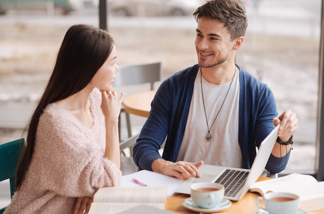 This our profit. Handsome youthful man presenting some information to his female partner while sitting at cafeteria during lunch break.