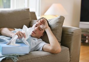 Man with a cold lying in sofa holding tissues
