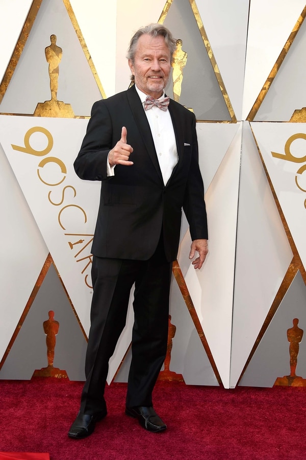 John Savage un clásico traje negro con zapatos cerrados con punta cuadrada destacando de su look la elección del moño estampado en rojo, blanco y gris