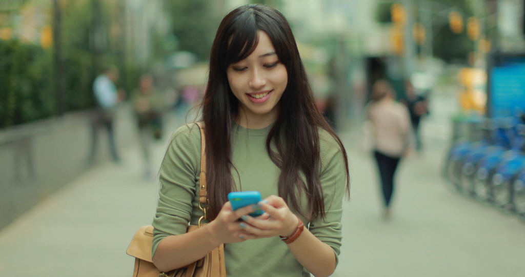 young-asian-woman-walking-texting-smart-phone-cellphone-in-city-4k_nkitrvhx__f0000
