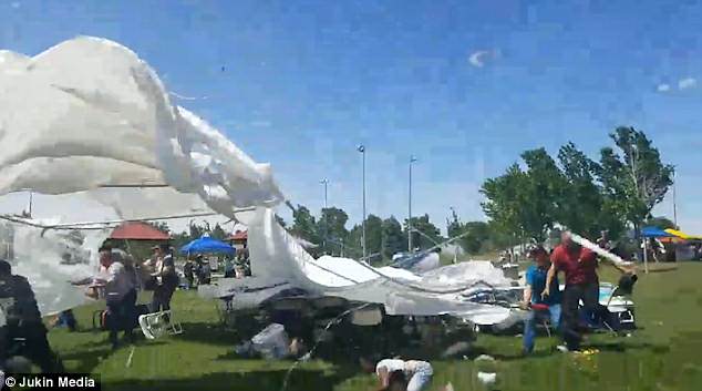 While a canopy hangs on by its few remaining pegs seemingly seconds away from flying into the air before a group of men hold onto it desperately