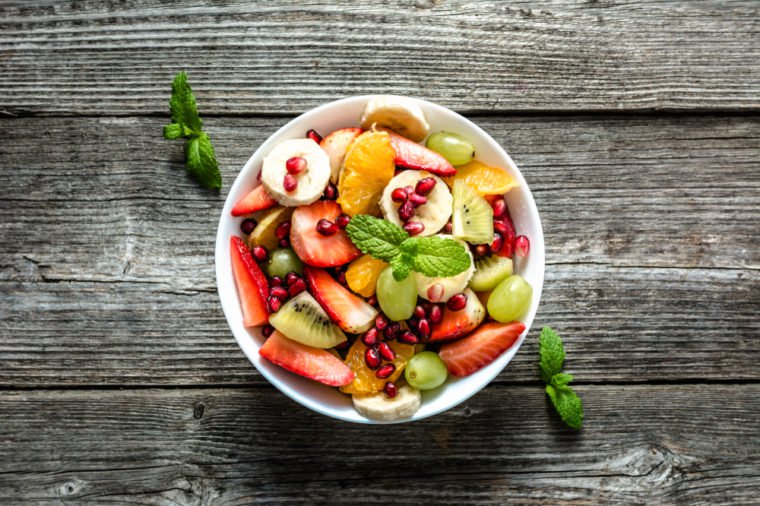 Fresh fruit salad, top view in a bowl on wooden background, vegetarian food concept
