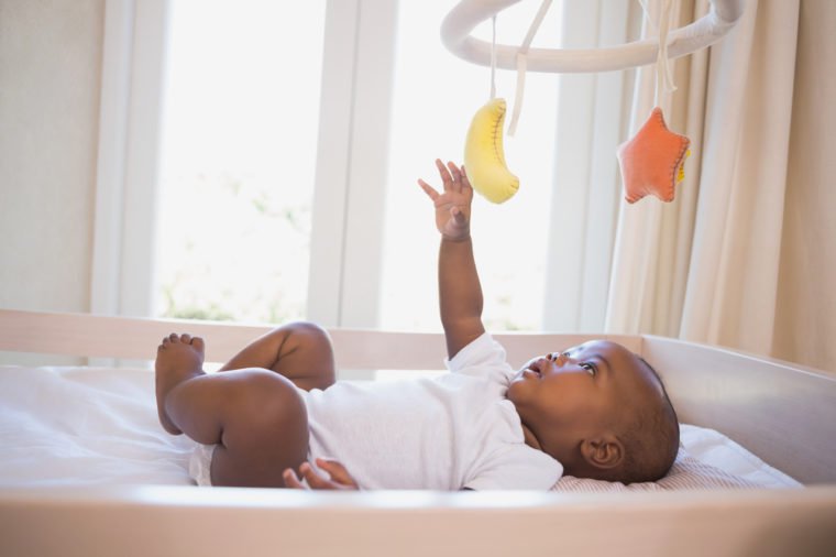 Adorable baby boy lying in his crib playing with mobile at home in the bedroom