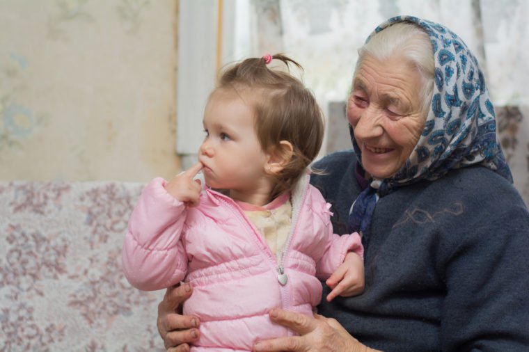 An elderly grandmother holds a small beautiful baby on her wrinkled arms. family generation. Youth and old age