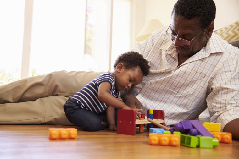 Grandfather And Grandson Playing With Toys On Floor At Home