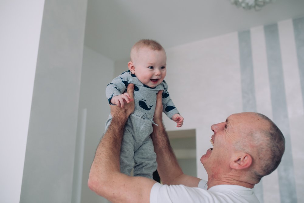 Grandfather holds granddaughter on hands. mother playing with her daughter