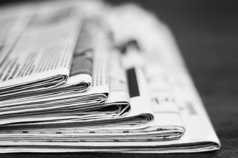 News - Pile of newspapers. Daily papers with articles and headlines stacked on the table. Actual information in press, fresh media. Folded tabloid pages on desk in office, data on paper. Side view