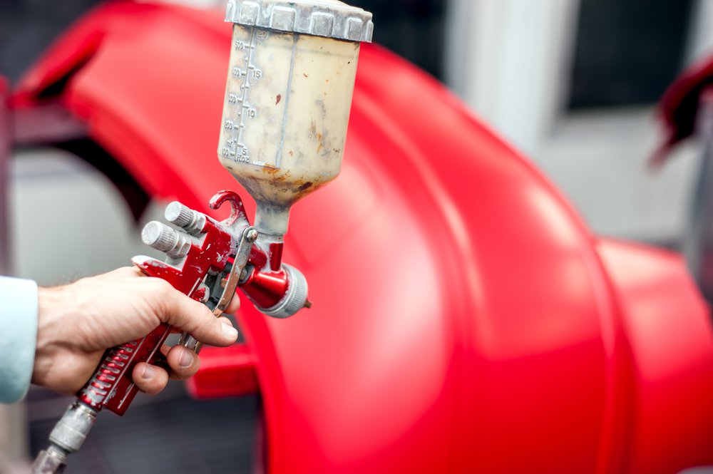 Close-up of spray gun with red paint painting a car in special booth