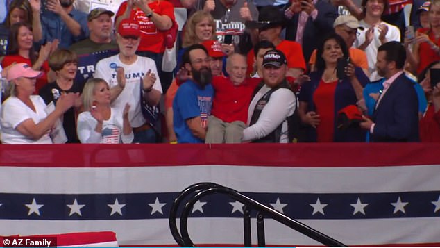 The heartwarming video shared on Twitter shows two men--one wearing a Trump hat--carrying the elderly man down a flight of stairs and across Arizona Veterans Memorial Coliseum as crowds cheered and chanted 