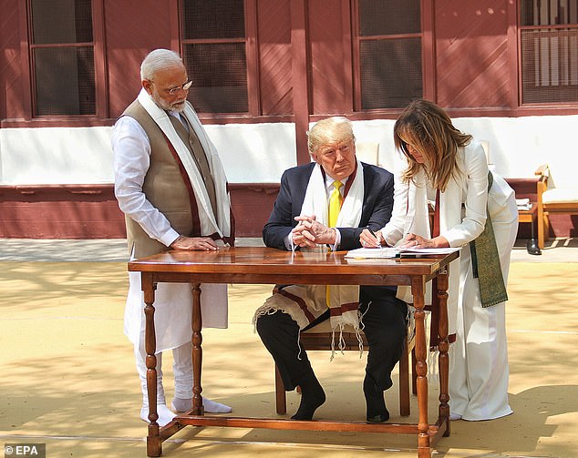 Melania Trump, in a prayer shawl and slippers, sins the guest book at Gandhi