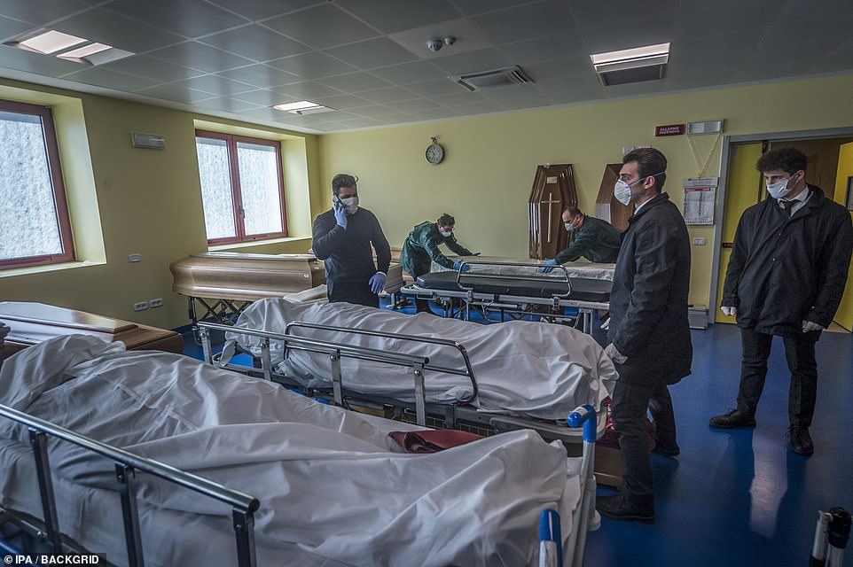 Hospital workers in face masks stand over trolleys at the Ponte San Pietro hospital in Bergamo on Tuesday as they prepare coffins