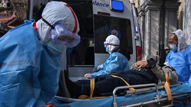 Medical staff carry a suspected COVID-19 patient in Wuhan in January as cases surged. The city has now revised the death toll [Hector Retamal/AFP]
