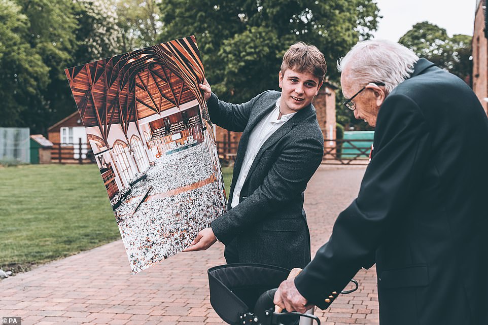 Benjie Ingram-Moore, 16, presenting his grandfather Captain Tom Moore with a photograph of the Great Hall of Bedford School, Bedfordshire, filled with cards for his 100th birthday