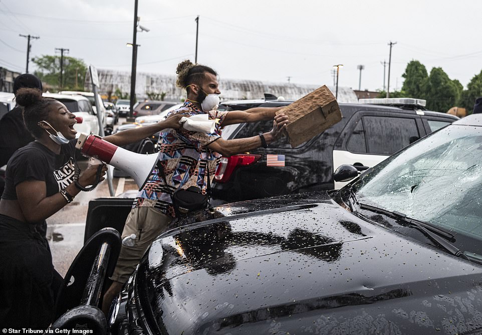 A protesters smashes the window of a police squad car as hundreds converge on a police precinct in Minneapolis in anger at the death of George Floyd after a police officer kneeled on his neck before he died