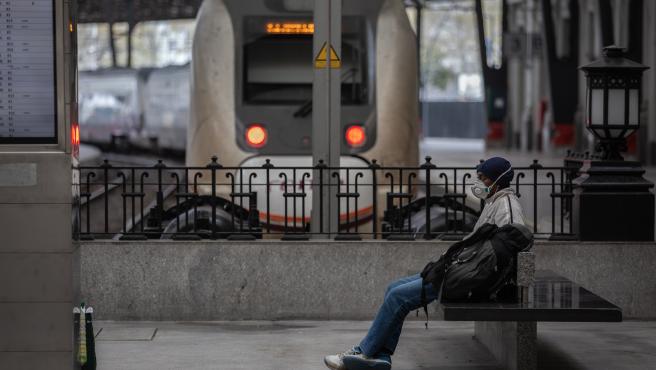 Un hombre protegido con una mascarilla espera sentado en un banco en una estación de tren de Barcelona durante el segundo día laborable del estado de alarma por el coronavirus, en Barcelona (España), a 17 de marzo de 2020.