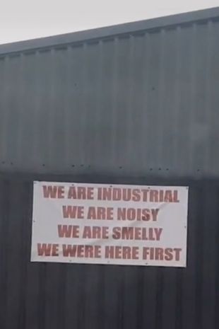 The sign warns residents: “We are industrial. We are noisy. We are smelly. We were here first.”